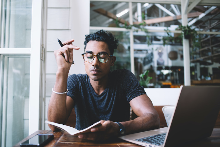 man focused on his notes next to his laptop