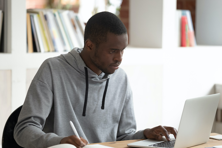 african american taking notes from his laptop in a school library