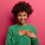 woman in a green sweater standing against pink background