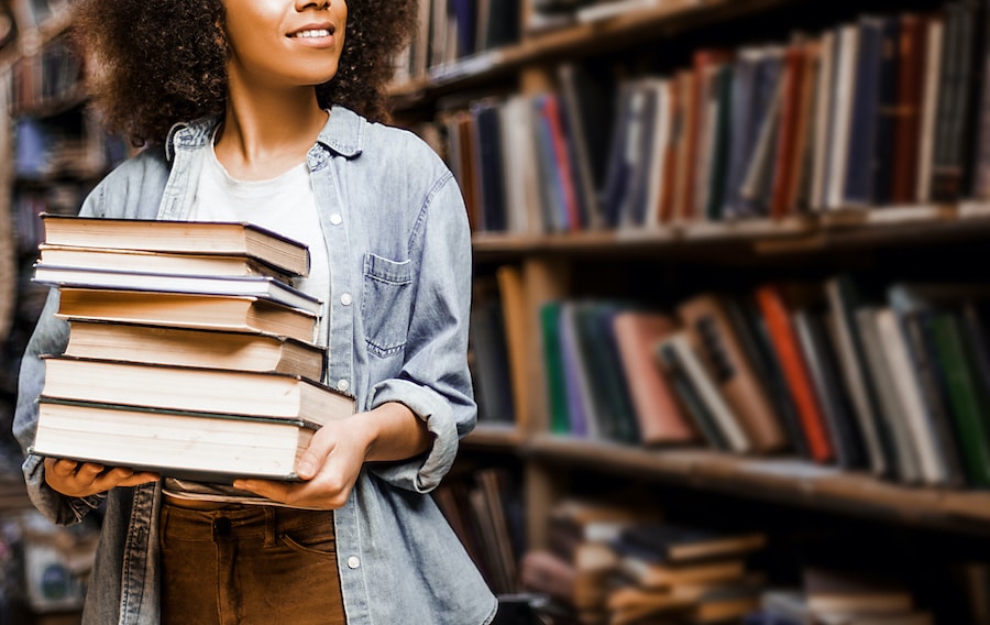 woman with curly hair holding a stack of books in a library