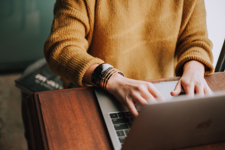 woman in a yellow sweater typing on her laptop