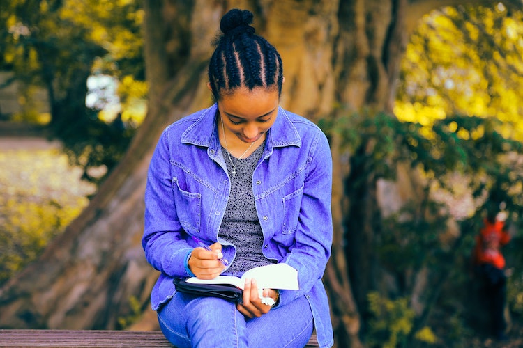 african american woman writing in a notebook outdoors
