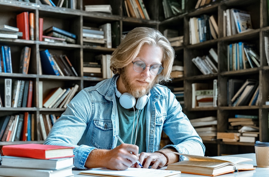 blonde man with eyeglasses taking notes in a library