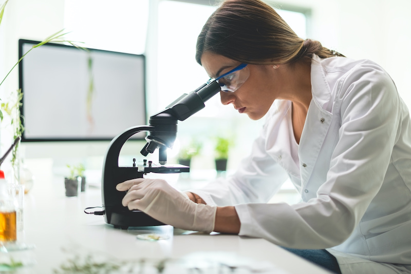 woman in lab coat inspecting something through microscope
