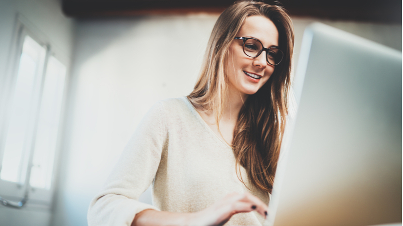 woman with long hair and eyeglasses typing on her laptop