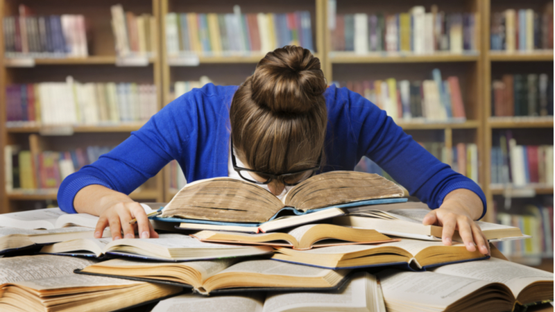 stressed out student with his head down in a book in the library