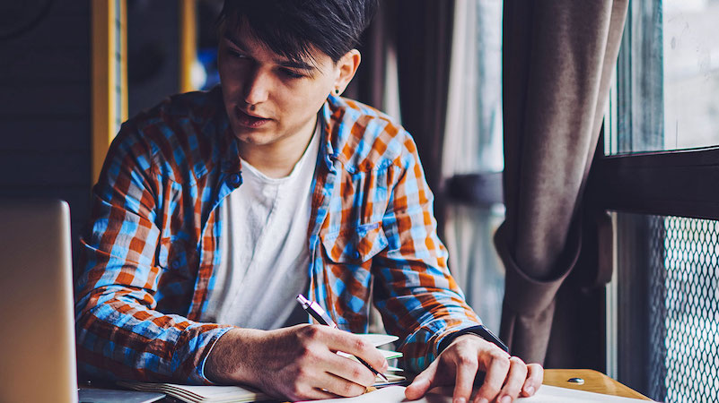 man taking notes from a laptop next to the window