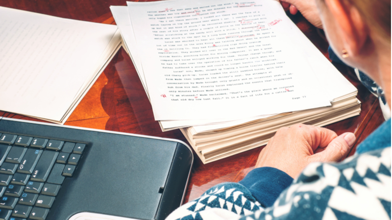 woman revising a stack of papers with a computer