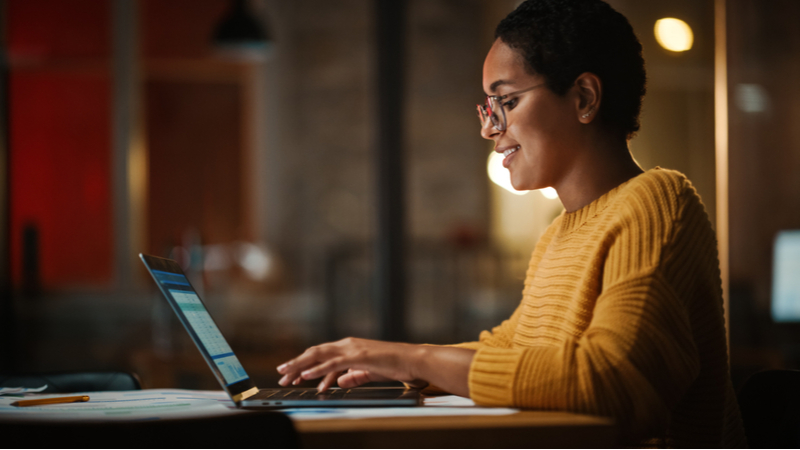 Black woman smiling while working on her laptop in a home office