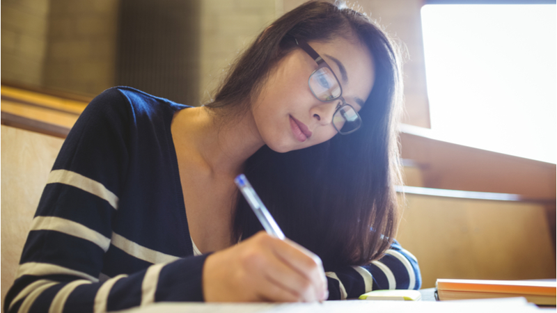 woman with glasses writing down notes in a college auditorium