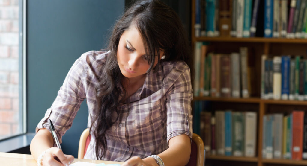 woman writing a dissertation abstract in library