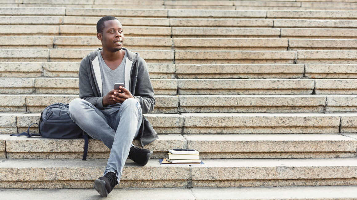 black student sitting alone on campus stairs with books next to him