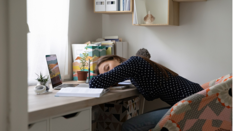 woman sleeping on her desk with open laptop and books
