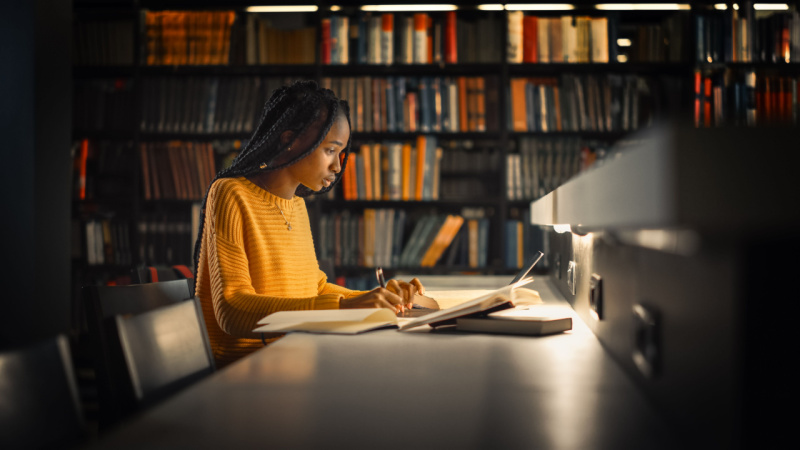 woman studying in the library at night under a desk light