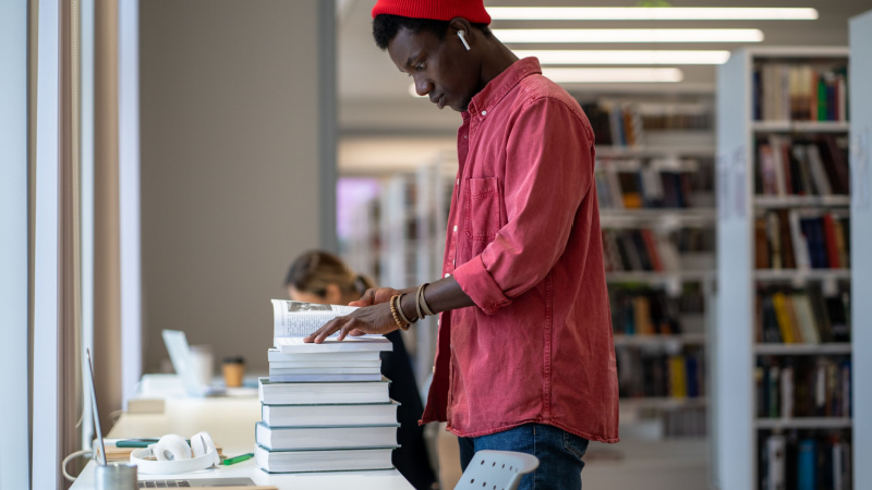 African American grad student standing at desk with pile of books