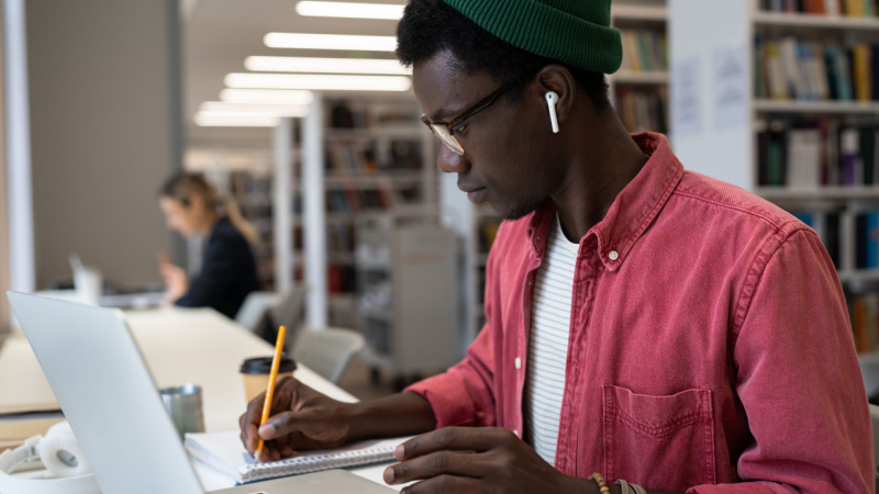 focused african american grad student taking notes in front of laptop